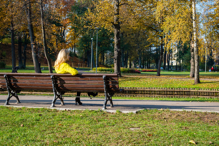 A young, beautiful, blonde woman sitting in a park on a bench.の写真素材