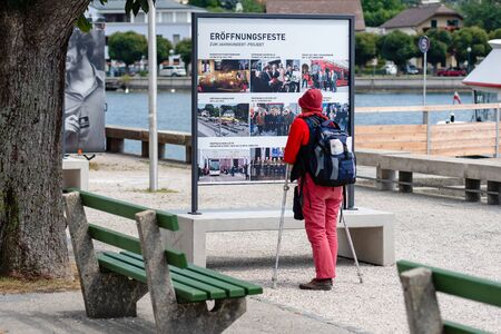 GMUNDEN, AUSTRIA, - AUGUST 03, 2018: A woman with crutches and a backpack stops at the billboard and reads.のeditorial素材