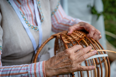 Old woman in national costume make local wicker basket. Traditional handicrafts concept. Latvia -...