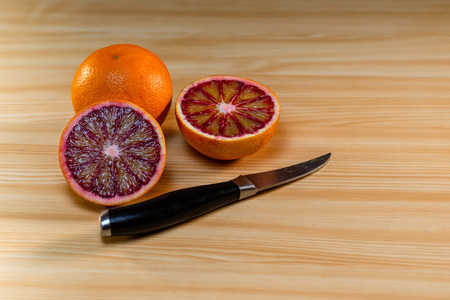 Glass of juice, knife and cut red oranges on a light wooden table.の写真素材