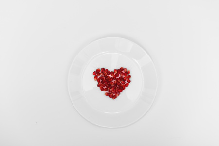 On a white plate from pomegranate seeds composite heart shape. White background. Flat layer.の写真素材