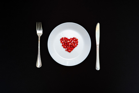 On a white plate from pomegranate seeds composite heart shape. Knife and fork next to the plate....