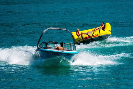 WORTHERSEE, AUSTRIA - AUGUST 08, 2018:  Happy young people, on inflatable attractions, drive behind a motorboat on the lake.のeditorial素材