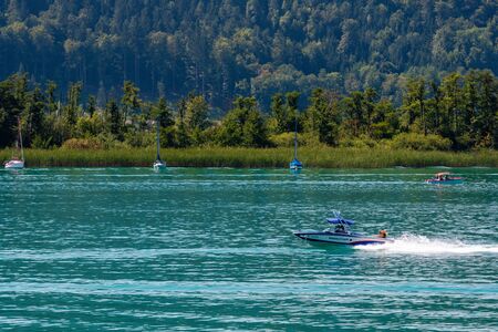 WORTHERSEE, AUSTRIA - AUGUST 08, 2018: View from the boat to the lake and coastline. Local residents and tourists swim, driven by motorboats and use other forms of water recreation.のeditorial素材
