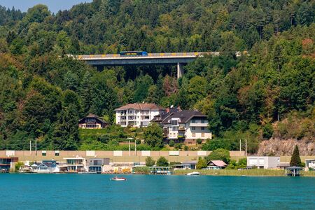 WORTHERSEE, AUSTRIA - AUGUST 08, 2018:  Great scenery from the boat to the shore line of the lake, beautiful buildings, mountains, forests, highways. Tourists who enjoy a variety of water recreation types.のeditorial素材