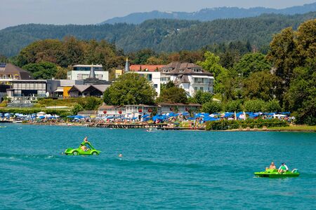 WORTHERSEE, AUSTRIA - AUGUST 08, 2018:  Great scenery from the boat to the shore line of the lake, beautiful buildings, mountains, forests, highways. Tourists who enjoy a variety of water recreation types.のeditorial素材
