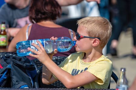 WORTHERSEE, AUSTRIA - AUGUST 08, 2018:  A blond boy on a hot day drinks water from a plastic bottle.