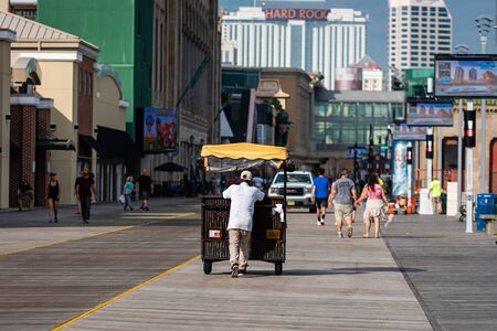 ATLANTIC CITY, NEW JERSEY - JUNE 18, 2019: A pedicab pushes his customers past the Boardwalk lined with restaurants, shop and casino.のeditorial素材