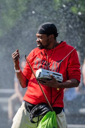 New York, USA - June 21, 2019:  In a fountain in a public park, a black man in red clothes performs...