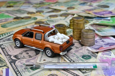 Thermometer and toy pickup with tablets in a cargo box on background of different countries currency banknotes. The concept of medical availability and increasing medical expenses - imageの写真素材