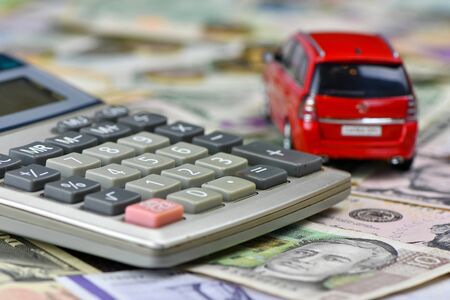 Calculator and red toy car on a variety of national currency banknotes background.  Concept of the cost of purchasing, renting and maintaining a car  - imageの写真素材