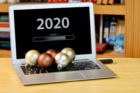 on the table laptop with text - 2020 loading - on screen and with christmas decorations  on the keyboard, blurred shelf with books in the background - imageの写真素材