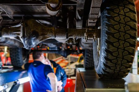 Riga, Latvia - April 12, 2019: A mechanic is checking the technical state underneath a lifted car on a bridge in a garage - imageのeditorial素材