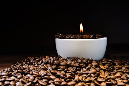 White coffee cup full of coffee beans and burning candle on top of coffee bean stack - imageの写真素材
