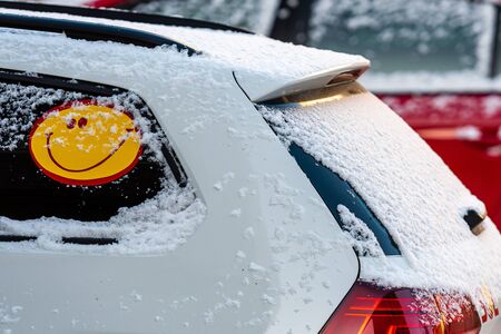 Close-up of a white, snowy car with a smiley sticker - image