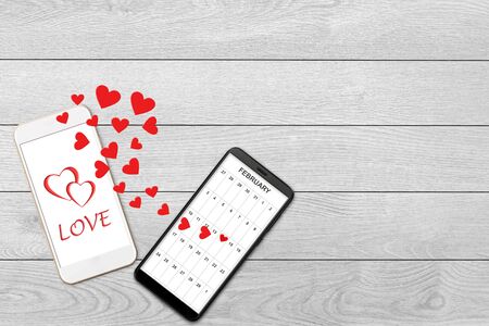 Valentine day concept, love message - hearts flying out of two smartphones, Isolated on white wooden background, calendar and greeting on smartphone screenの写真素材
