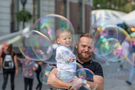 Old Town Square, Riga, Latvia - August 16, 2019: Bearded man with a child on his hands watches and rejoices at the gigantic soap bubblesのeditorial素材