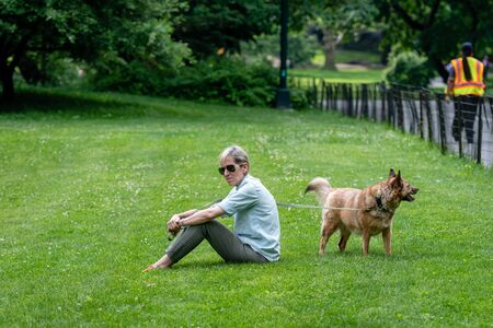 New York, USA - June 6, 2019:  A woman with a dog sits on a lawn in Central Park.のeditorial素材