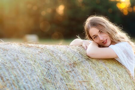 Emotional portrait of a cheerful  blonde girl in a countryside landscape with hay rolls in sunset light - imageの写真素材