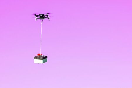 multicopter drone flying with a gift box isolated on a pink background, concept of modern fast delivery method by using dronesの写真素材