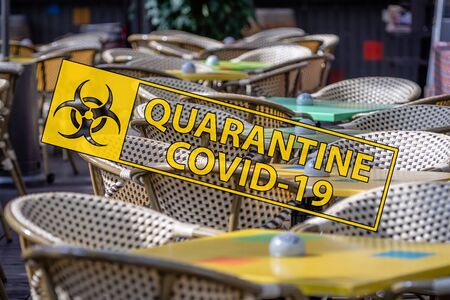 Covid-19 quarantine sign on the background of an empty wicker chairs and colorful tables in the outdoor cafeの写真素材