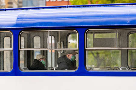 Riga, Latvia - May 14, 2020: tram passengers ride in medical masks, side view through the window of a half-empty public transport on a man and a woman, coronavirus Preventionのeditorial素材
