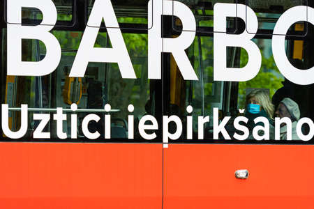 Riga, Latvia - May 14, 2020: woman is seen through the window of a public tram wearing a face mask to protect from Coronavirusのeditorial素材