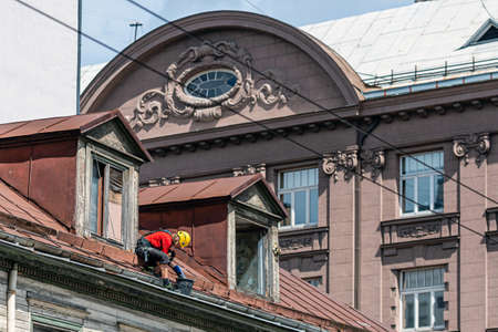 Riga, Latvia- July 3, 2020:  Industrial climber removes leaves and dirt from house rooftop rain gutterのeditorial素材