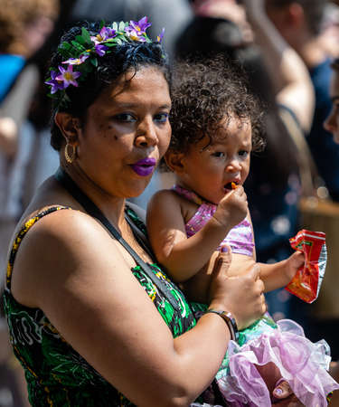 New York, USA - June 22, 2019: African woman with a flower wreath on her head and a baby on her hands walking in the crowd on the streetのeditorial素材