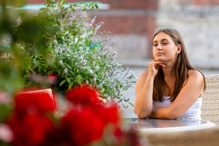 young beautiful woman sitting at table of street cafe and waiting for meeting, defocused flowers in the foregroundの写真素材