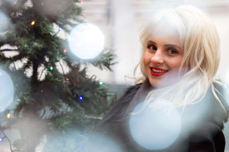 Portrait of a young smiling blonde woman photographed through the Christmas lights, soft focus - imageの写真素材