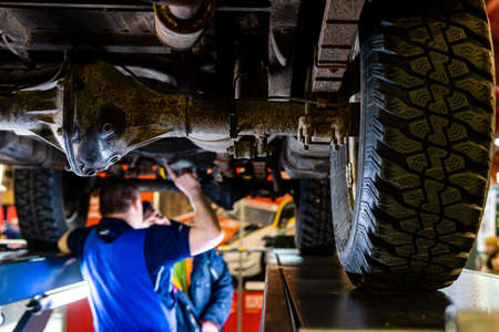 Riga, Latvia - April 12, 2019: A mechanic is checking the technical state underneath a lifted car on a bridge in a garage - imageのeditorial素材