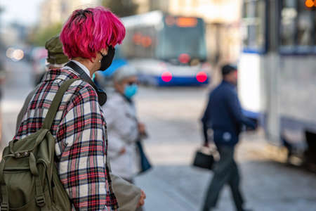 Riga, Latvia - October 8, 2020: a young man with red hair and a medical mask on his face is waiting for public transport on the street, preventive measures for the spread of coronavirusのeditorial素材