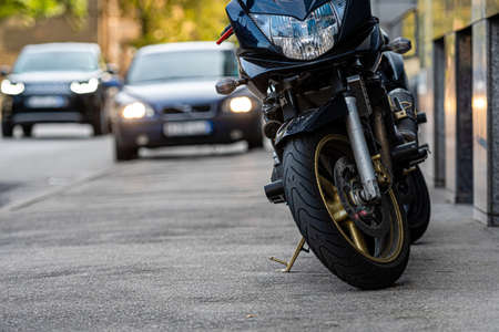 a motorcycle parked on the sidewalk with a blurred city street with cars in the background, selective focusの写真素材