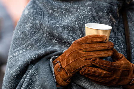 hot drink in paper cups for beverages with a takeaway (tea or coffee) in hands with gloves, close-up