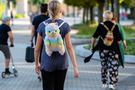 A girl with a colored backpack-bear goes down the street. Rear view.の写真素材