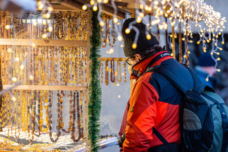 Riga, Latvia, December 1, 2019: a man in a winter jacket and a backpack at a souvenir kiosk at the Christmas marketのeditorial素材