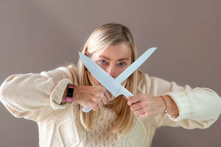 blonde woman gesticulates emotional with knifes, isolated on a dark background