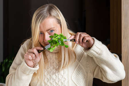 middle aged blonde woman eating salad in the kitchen, healthy food conceptの写真素材