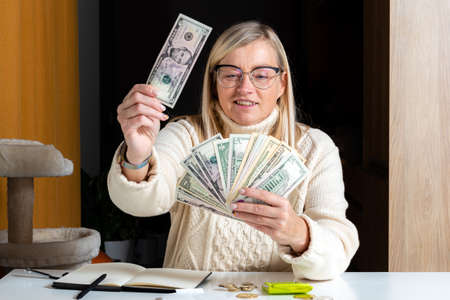surprised woman sitting at a table and looking at dollar bills and enjoying the money earned,...