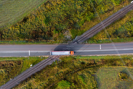 aerial view of railroad tracks crossing a asphalt road with cars in rural areaの写真素材