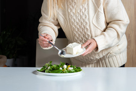 middle aged blonde woman preparing green salad in the kitchen, healthy eating and diet concept,...