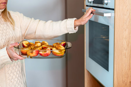 woman puts glass containers with sliced stuffed apples in the oven, homemade dessert conceptの写真素材