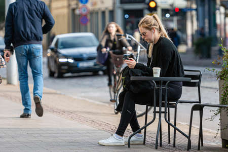 Riga, Latvia - October 8, 2020: a young woman in sunglasses sits at a table on the sidewalk on the side of the street and drinks coffeeのeditorial素材