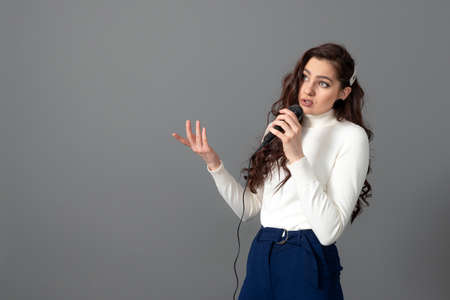 attractive female conference speaker during presentation, holds microphone and makes some gestures, isolated on grayの写真素材