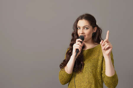 attractive teenager woman speaking with a microphone against gray background, speech presentation