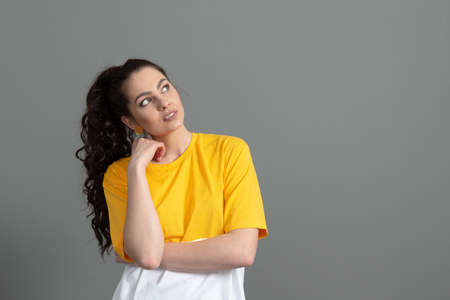 portrait of a young teenager with long wavy hair dressed in a yellow t-shirt, isolated on grayの写真素材