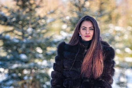 cheerful young woman in a warm fur coat enjoying a winter day in the snowy forest