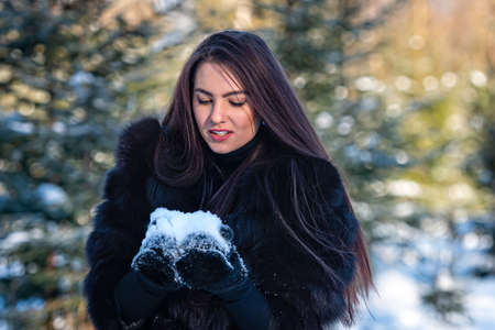 cheerful young woman in a warm fur coat enjoying a winter day in the snowy forestの写真素材