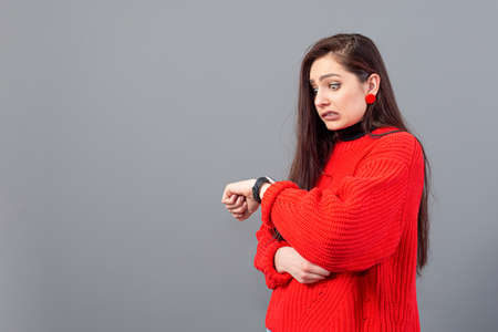busy woman in red sweather worried looking at her wristwatch, female being late, isolated on grayの写真素材